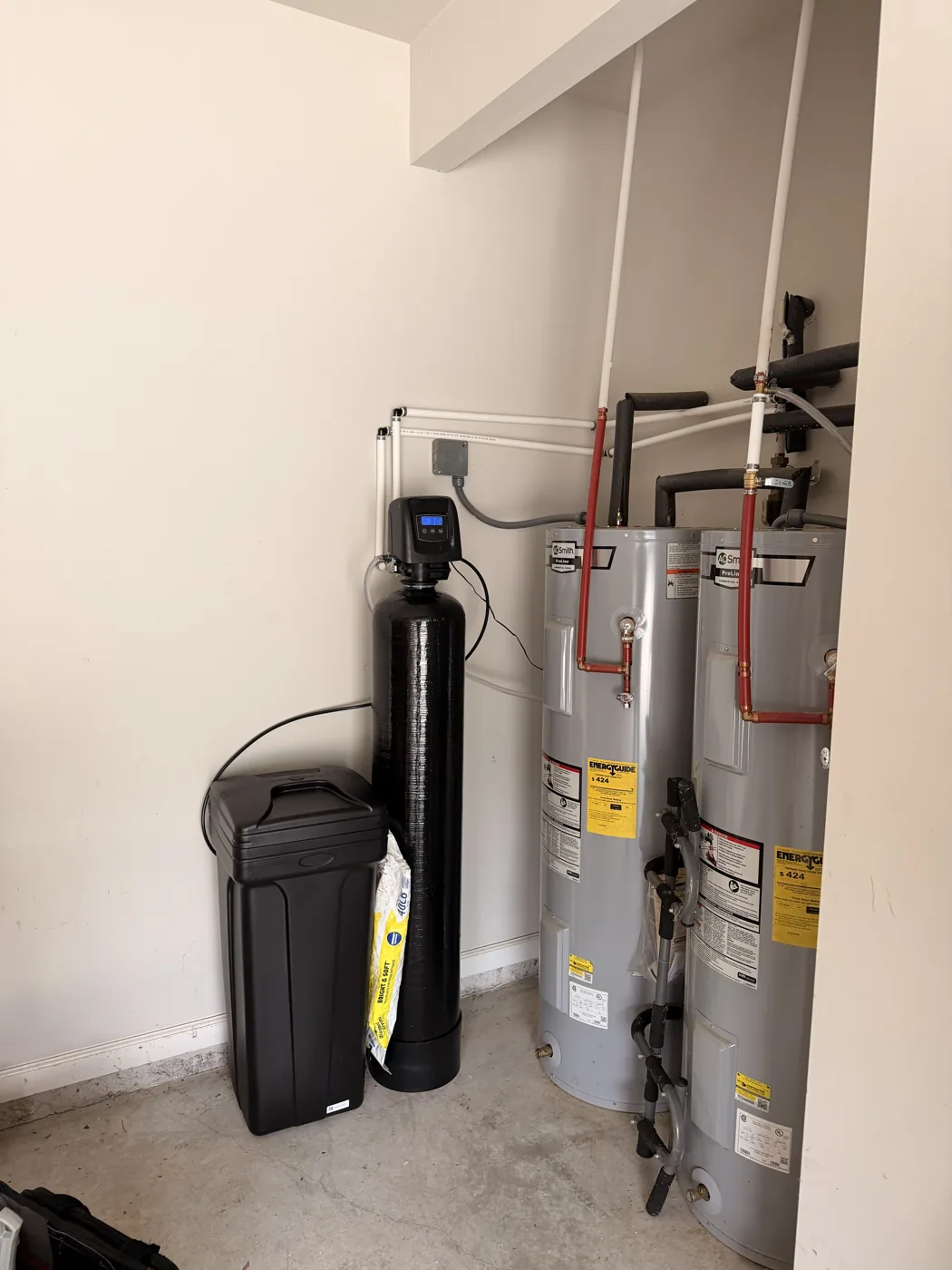 Installed whole-home water treatment tank and brine tank beside twin water heaters